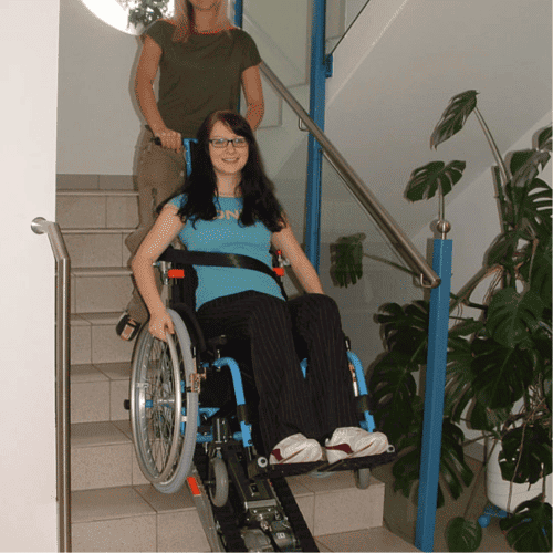 Frau im Rollstuhl wird komfortabel mittels Rollstuhlraupe die Treppe hinuntergefahren – sicherer Transport von GBK-Krankenfahrten.